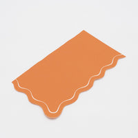 Two folded orange scalloped guest towels stacked, showing the wavy edge and cream outline detail.