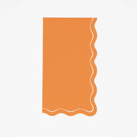 Orange fall paper guest towel in solid pumpkin with a cream wavy scalloped edge, flat view on white background.