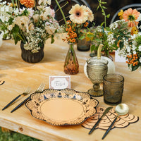 Orange fan-shaped spiderweb paper napkin with black web lines and a spider, set beside a scalloped Halloween plate with gold flatware