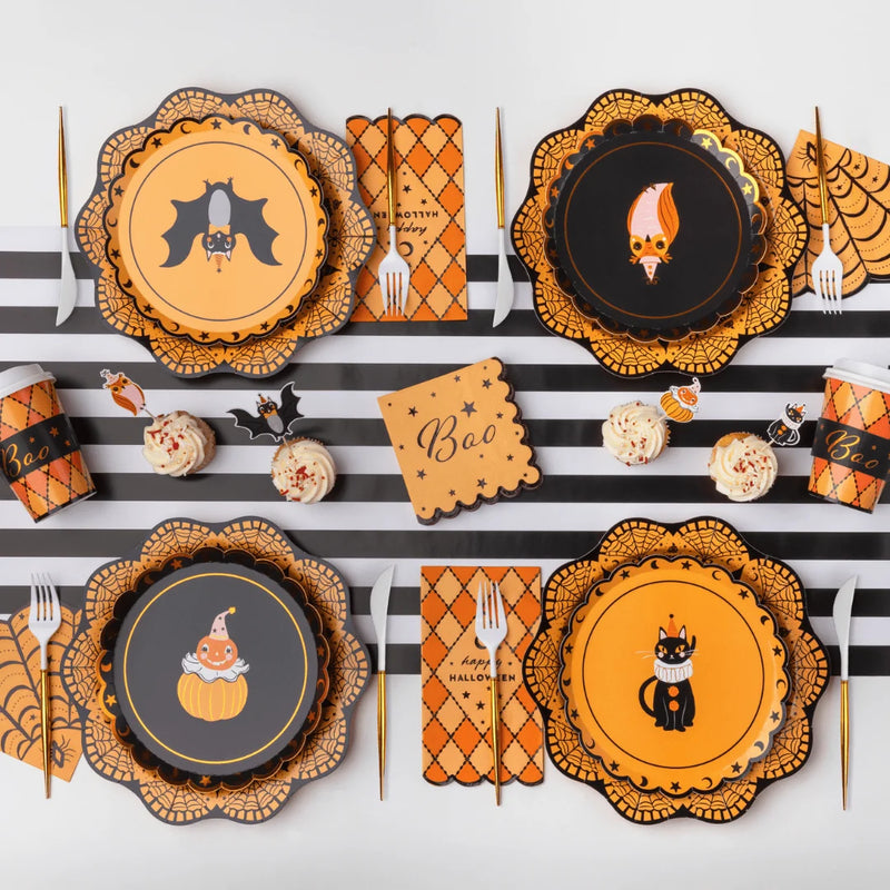 Orange spiderweb fan paper napkins tucked beside vintage Halloween character plates on a black and white striped runner