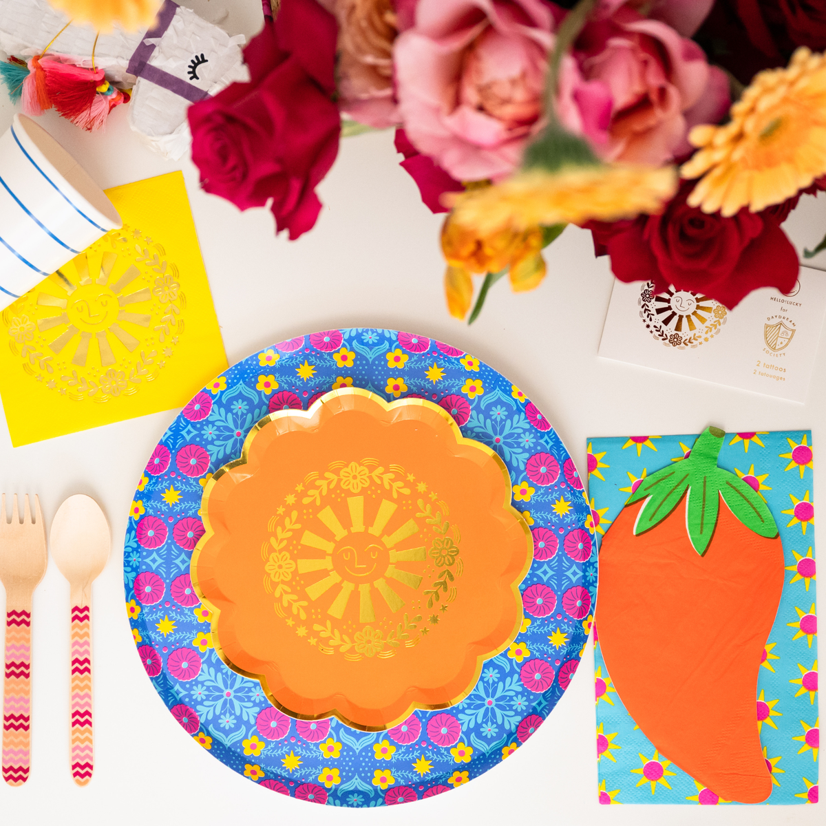 This image shows a vibrant fiesta place setting with an orange sun plate layered on a floral plate next to chili pepper napkins.
