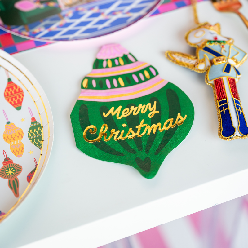 The ornament napkin styled on a holiday table beside a plate, a nutcracker figure, and colorful Christmas décor.