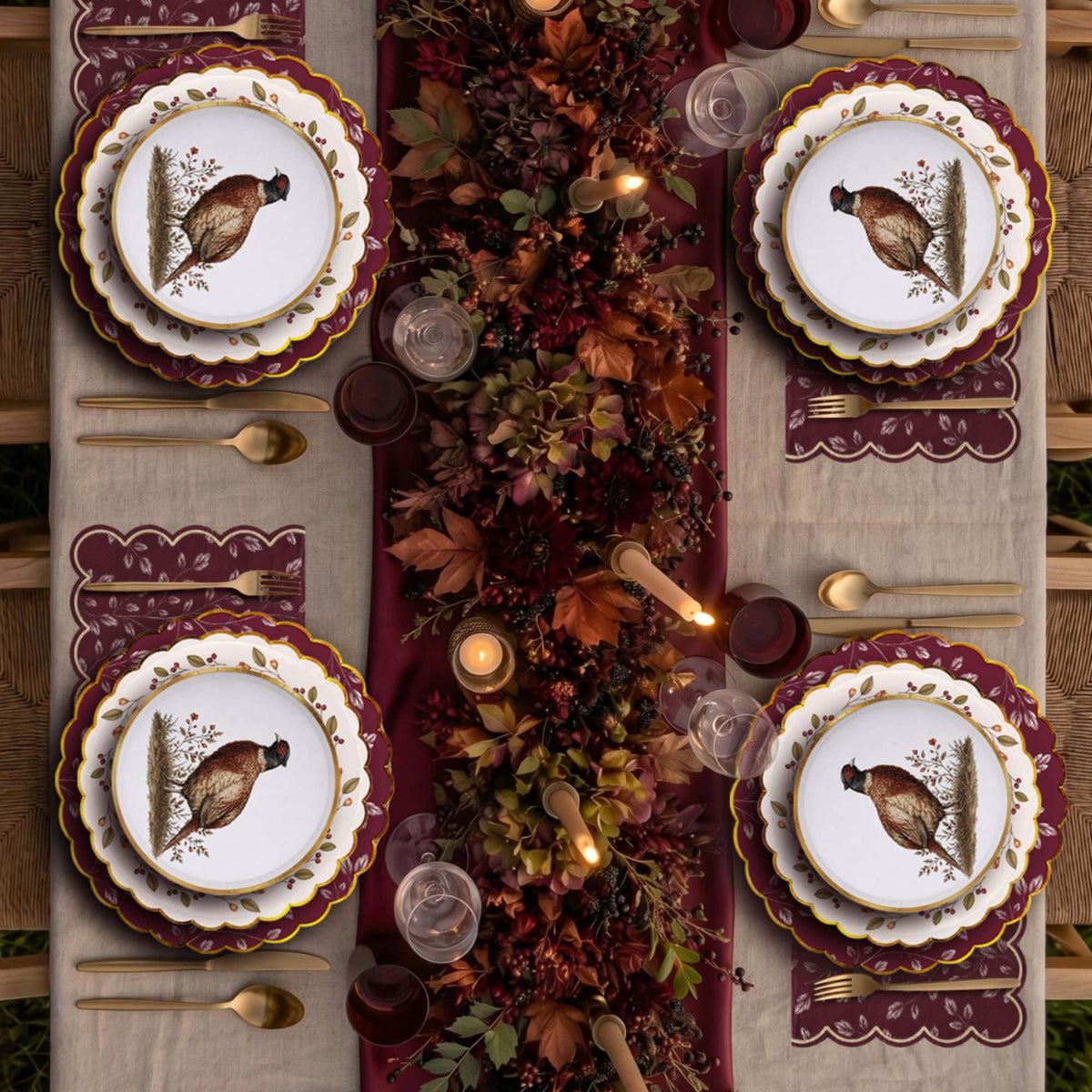 Outdoor fall table for four with layered burgundy place settings, gold flatware, and a dark floral runner