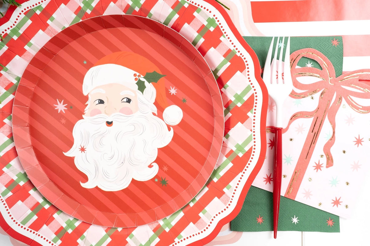 Wide overhead shot of a vintage Santa holiday plate setting layered on a plaid charger with matching festive tableware.
