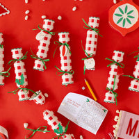 Overhead flat lay showing several Christmas crackers poppers, game cards, dice, and crowns on a red background.