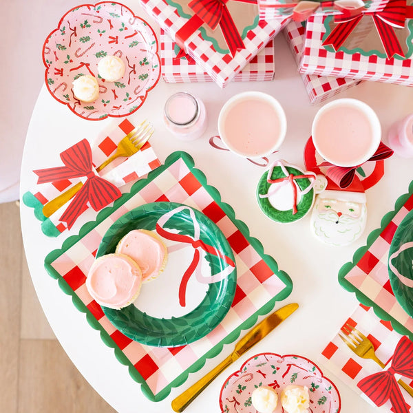 Overhead view of a table setting featuring the Christmas napkins, layered green and plaid plates, and pink drinks.