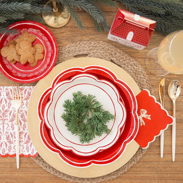 Overhead view of a detailed red and white tableware place setting with a Red Christmas Napkin, gold cutlery, and layered plates.