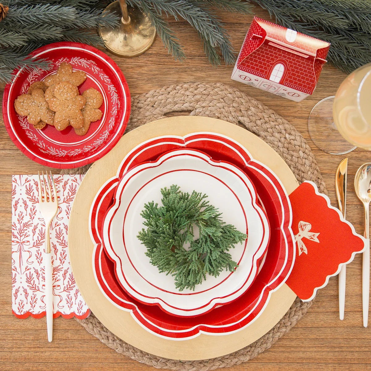 Overhead view of a holiday table with large holiday plates used as chargers, layered with smaller plates and greenery.