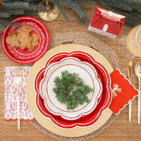 Overhead view of a holiday table with large holiday plates used as chargers, layered with smaller plates and greenery.