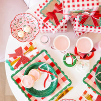 Overhead view of a party table set with candy cane tableware, including the pink plates, treats, and matching gift boxes.