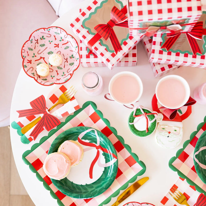 Overhead view of a party table set with candy cane tableware, including the pink plates, treats, and matching gift boxes.