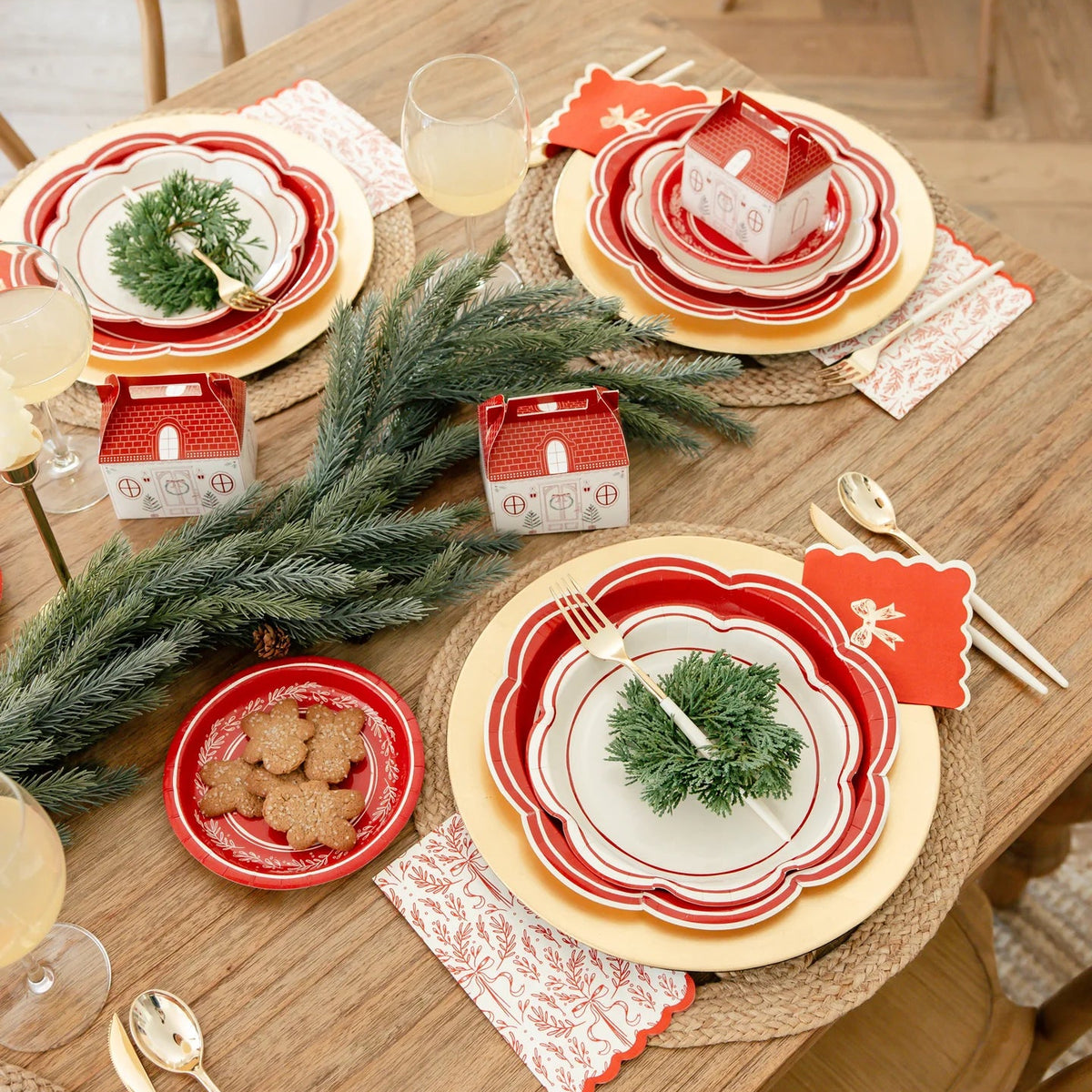Overhead view of a holiday table with large holiday plates used as chargers, layered with smaller plates and greenery.
