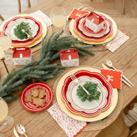 Overhead view of a holiday table with large holiday plates used as chargers, layered with smaller plates and greenery.