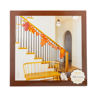Colorful oversized autumn leaves in orange, red, yellow, and gold draped along a white staircase railing with black iron balusters — fall staircase decorations.