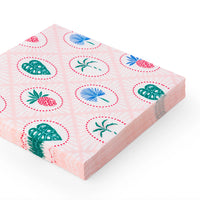 Angled stack of pink lunch napkins featuring tiny pineapples, monstera leaves, and palms.