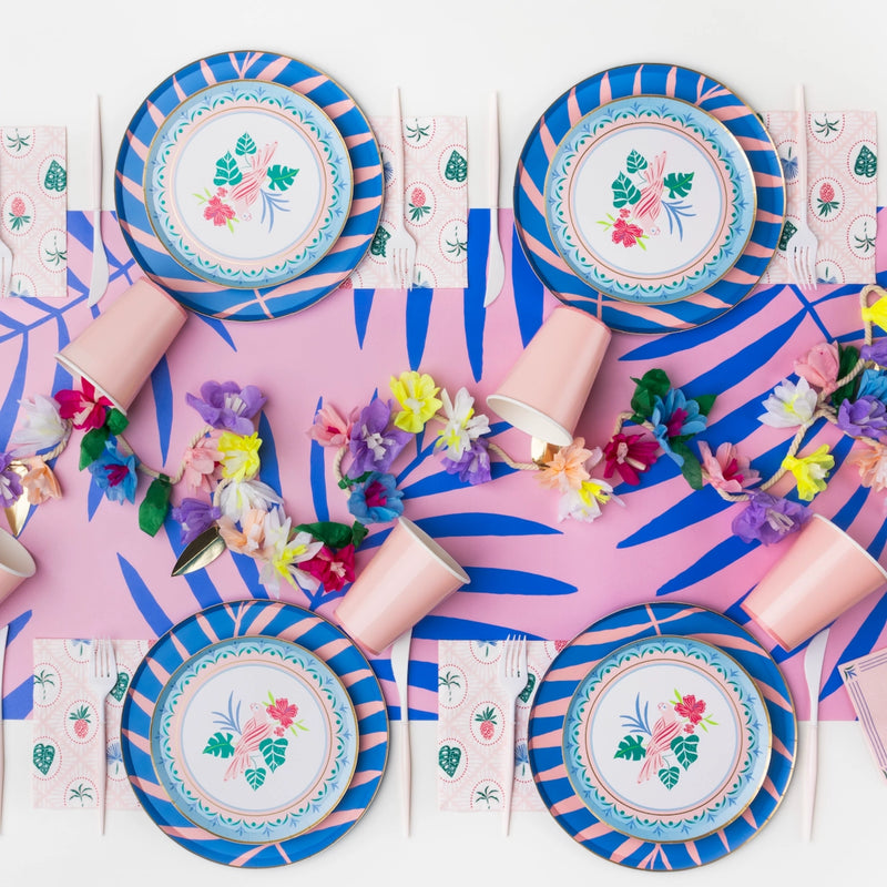 Tropical table with blue‑pink leaf runner, striped plates, and Palm Beach napkins at each setting.