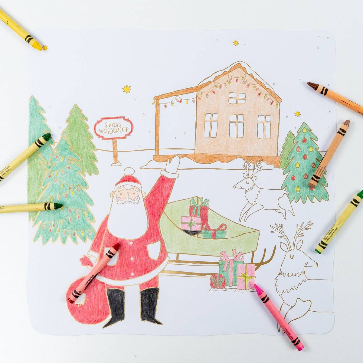 Overhead view of a partially colored winter village placemat surrounded by standard crayons.