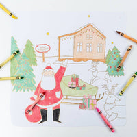 Overhead view of a partially colored winter village placemat surrounded by standard crayons.