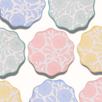 Overhead close-up of the four floral colorways overlapping, showing the block-print bloom and wavy scalloped edges.