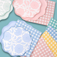 Pastel floral scalloped plates layered with coordinating pink, blue, and yellow gingham paper napkins.