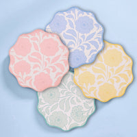 All four pastel floral scalloped paper plates in a flat-lay set on a blue background.