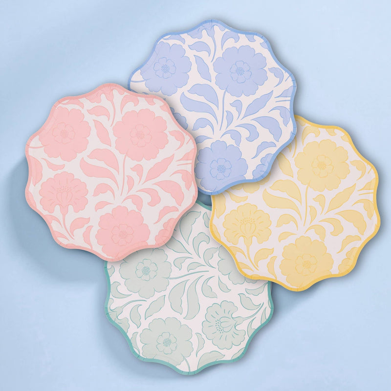 All four pastel floral scalloped paper plates in a flat-lay set on a blue background.