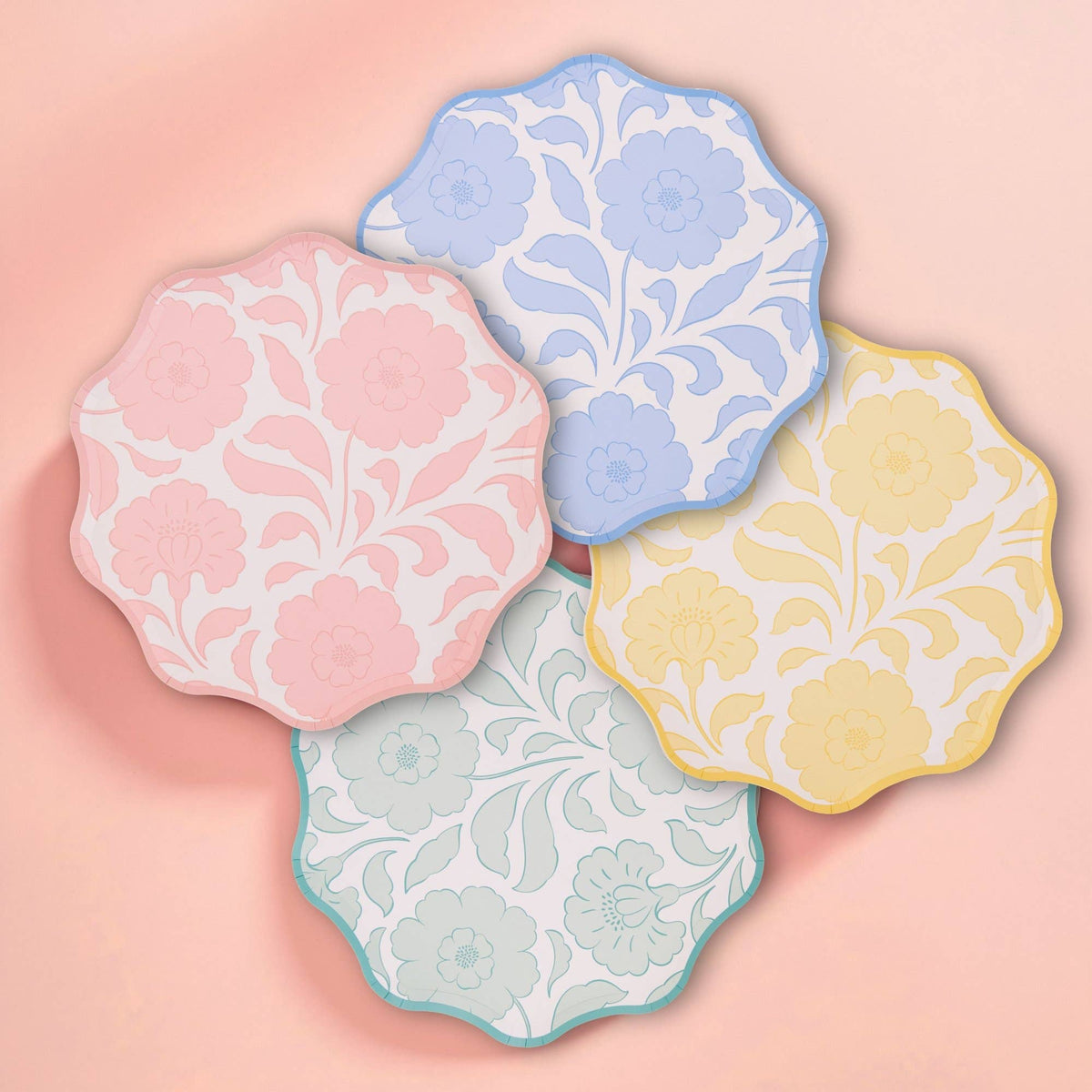 Pink, blue, yellow, and sage floral scalloped paper plates arranged on a peach background.