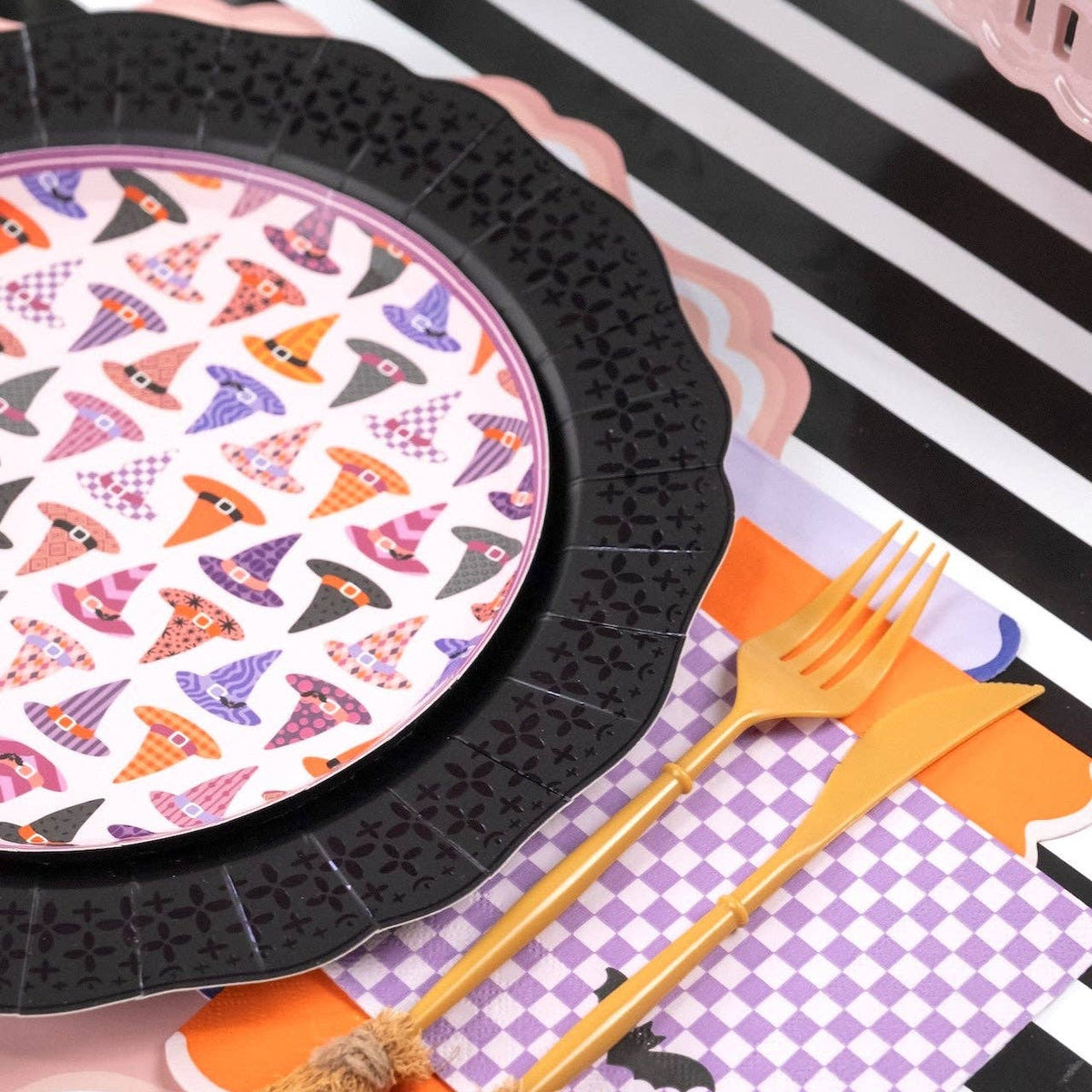 Angled overhead view of pastel purple and orange Halloween party tableware anchored by the black lace paper charger plates.