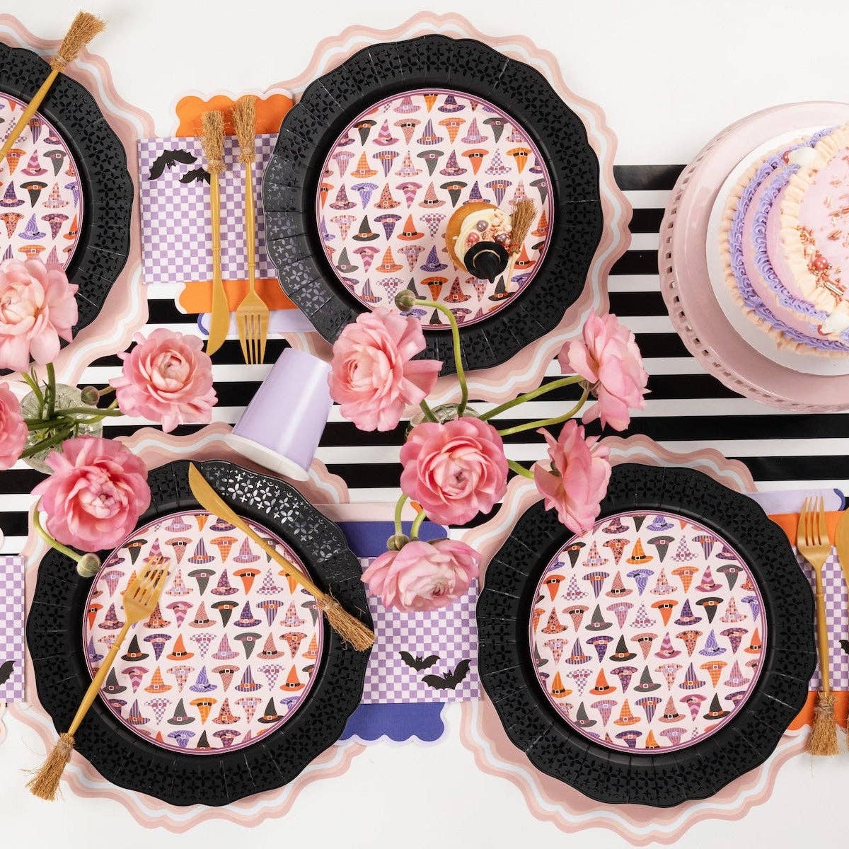Wide overhead shot of a pastel Halloween dinner party table with pink flowers and layered black die-cut plates.