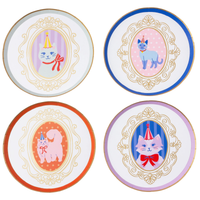 Top-down view of four round paper dessert plates, each featuring a pastel watercolor cat in a party hat inside a gold foil cameo frame with different colored borders.
