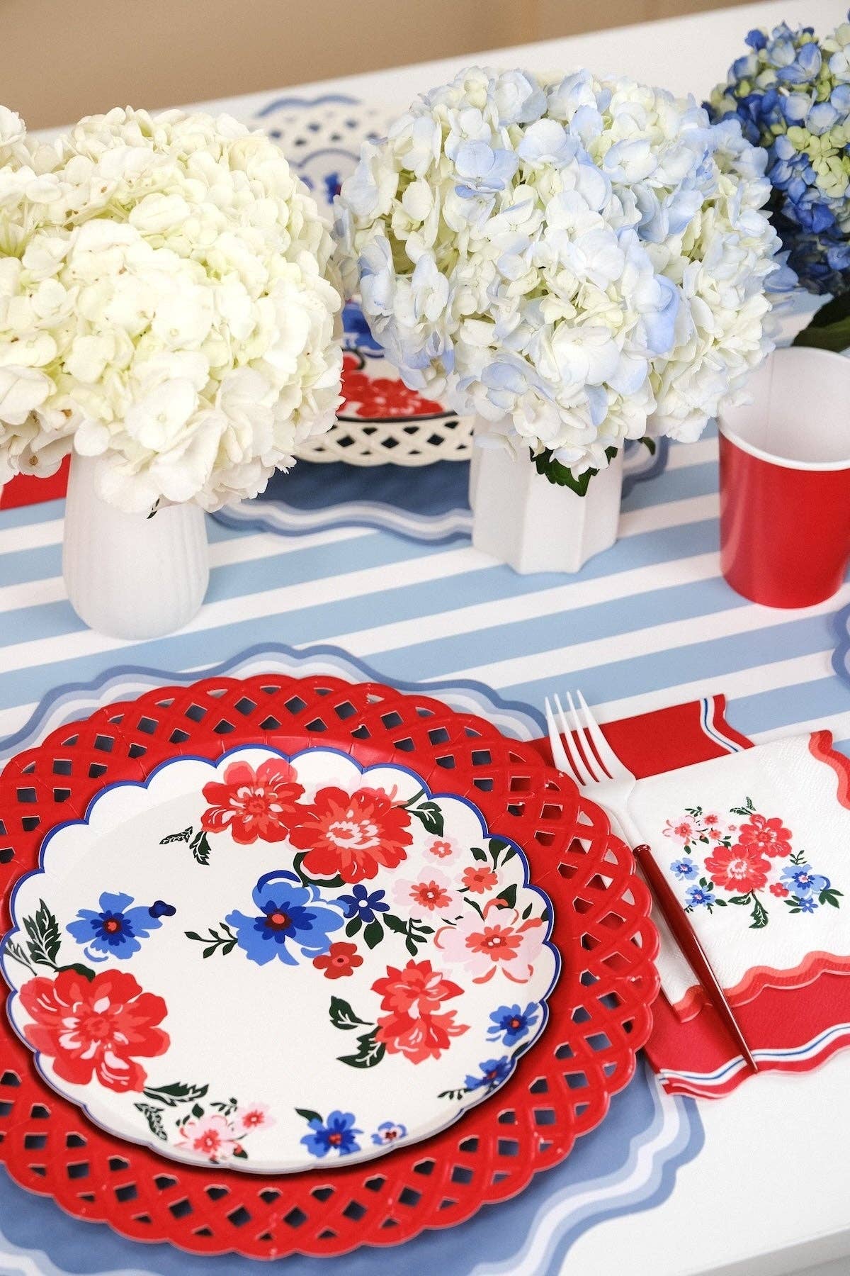 Side angle of Summer Floral Paper Plates on a blue-striped runner with red cups and florals.