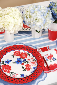 Side angle of Summer Floral Paper Plates on a blue-striped runner with red cups and florals.