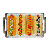 Full product shot of the hot dog platter-shaped paper plate on a white background. Rectangular shape with two silver foil cutout handles on each short end. Printed with four side-by-side hot dog illustrations on a light blue gingham ground: from left, a relish-mayo dog, a ketchup-strawberry dog, a mustard-ketchup swirl dog, and a Chicago-style dog with black olives and onion rings.