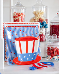 Close-up of patriotic party display shelf with stars and stripes square plates Uncle Sam hat shaped plate and rocket shaped napkins alongside glass candy jars