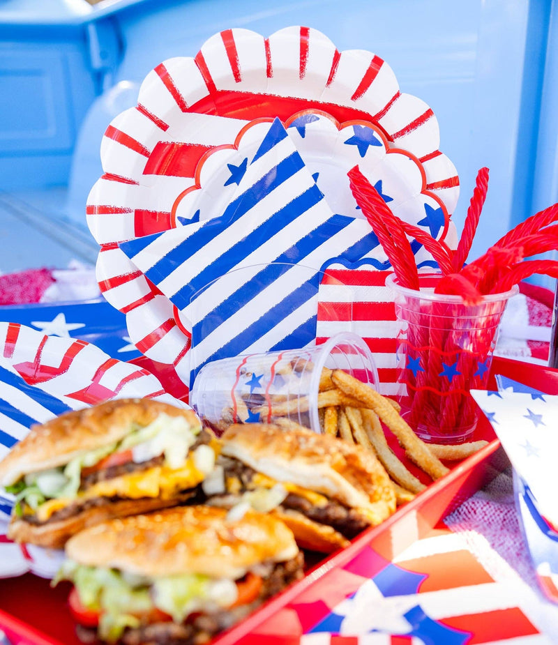 Close-up lifestyle photo of blue striped star shaped plates and red striped scalloped plates displayed with burgers fries and red licorice on a patriotic Fourth of July tablescape