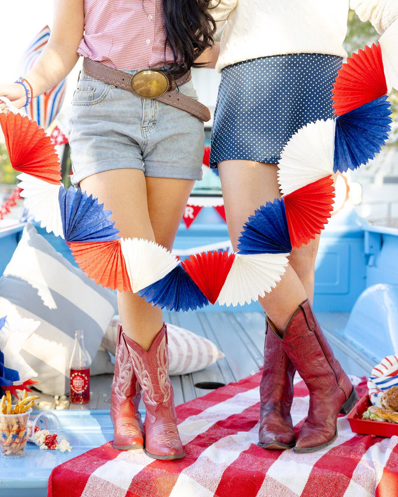 Close-up of two women holding red white and blue tissue fan bunting banner in vintage truck bed showing dimensional fan detail