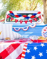 Red white and blue tissue fan bunting banner hung on vintage truck at a styled 4th of July picnic with American flag table runner and party supplies