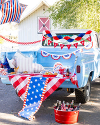 Red white and blue tissue fan bunting banner hung on blue vintage truck at 4th of July party with America felt pennant banner striped star balloon and patriotic decor