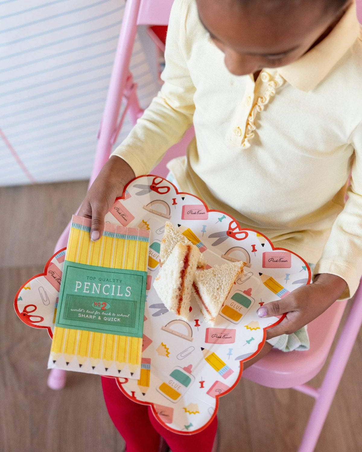 Young girl in yellow polo holding scalloped school supplies plate with PB&J sandwich and pencil box paper napkin