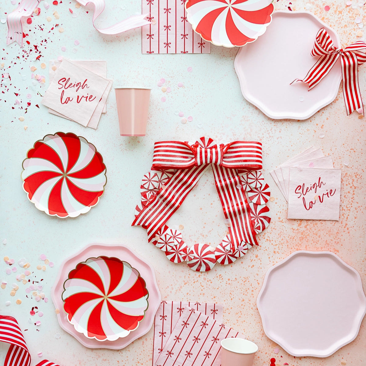 Party flatlay with petal pink compostable dinner plates styled with red peppermint plates and ribbons.