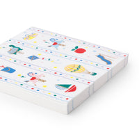 Close-up side view of stack of Petite Playground paper lunch napkins showing the classic toy print with carousel horse, hot air balloon, sailboat, kite, apple, spring turtle, and shooting star illustrations with gold foil accents and scalloped stripe borders