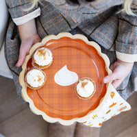 Person holding a pumpkin-shaped plate with small pumpkin pies on a wooden floor.