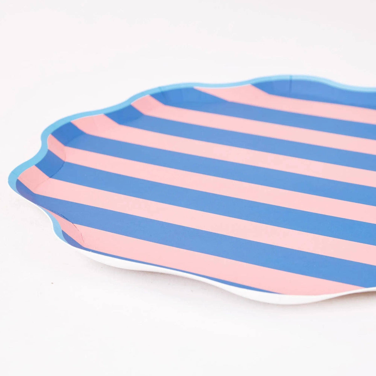 Angled close-up of a pink and blue cabana stripe scalloped plate showing the wavy edge and light blue border.