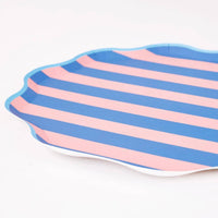 Angled close-up of a pink and blue cabana stripe scalloped plate showing the wavy edge and light blue border.