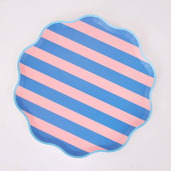 Pink and blue diagonal cabana stripe paper dinner plate with a wavy scalloped edge and light blue border, on a white background.