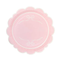 Single pink bow scalloped paper plate on white background showing pink surface with two white ribbon bow line drawings at top and bottom of inner circle, framed by a pink and cream scalloped flower-shaped edge