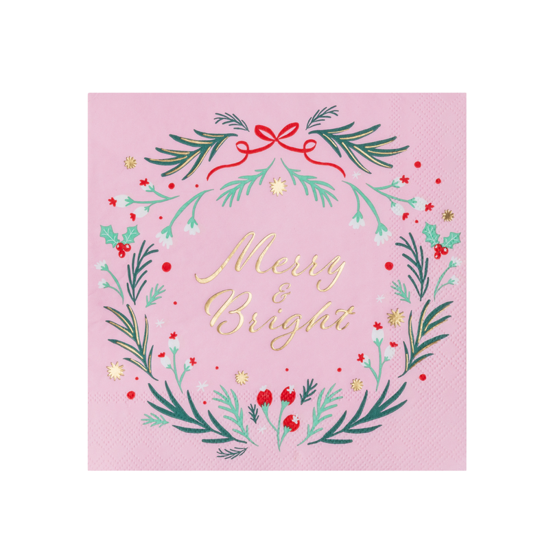 Flat pink Christmas napkin with a green wreath, red berries and a red bow circling gold "Merry & Bright" script on a blush ground.