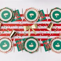 Styled pink Christmas tablescape showing the pink floral plates with coordinating wreath small plates, red-and-white striped runner, napkins, and a gold bow.
