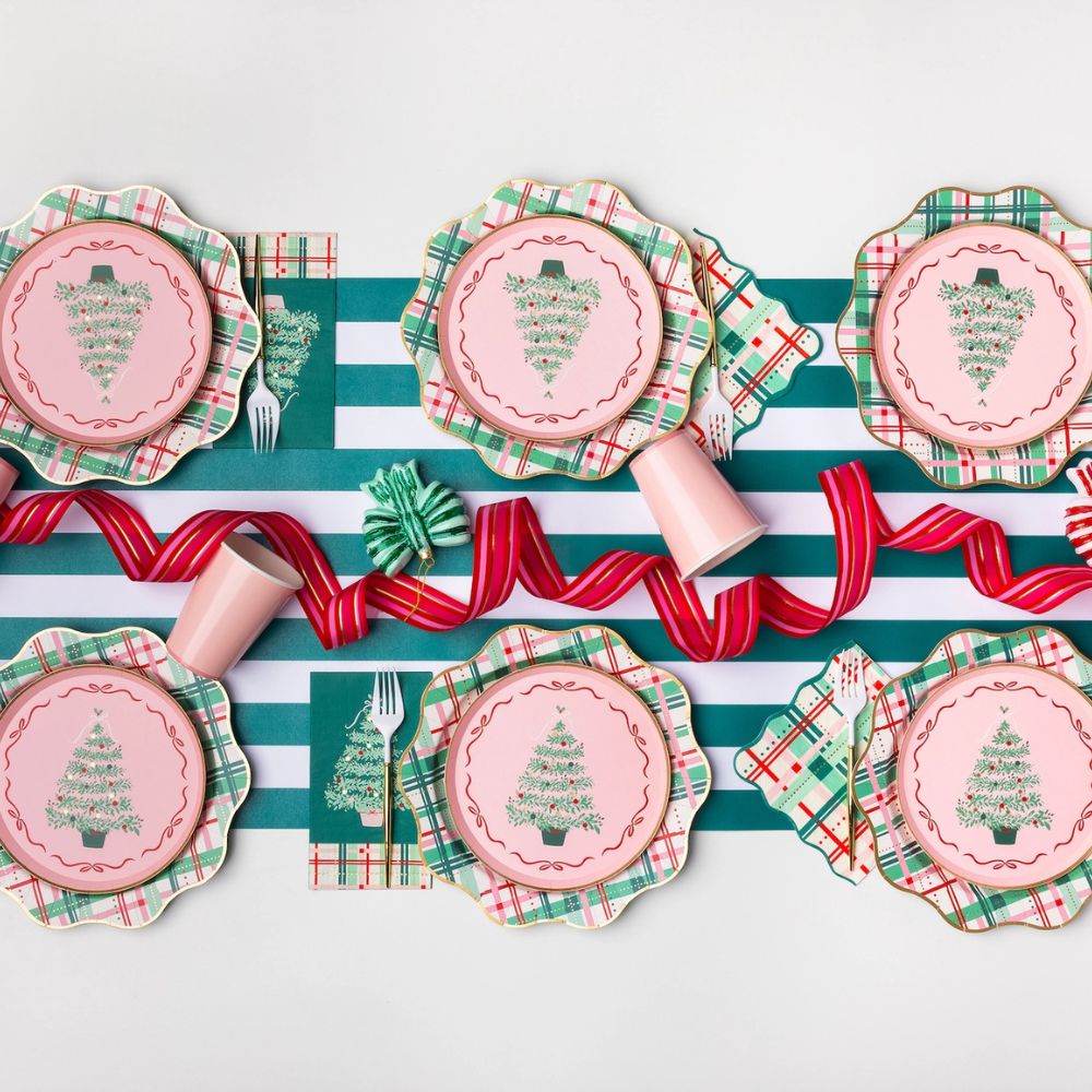 Festive Christmas tablescape featuring pink Christmas tree dessert plates layered over scalloped plaid dinner plates and other holiday tableware