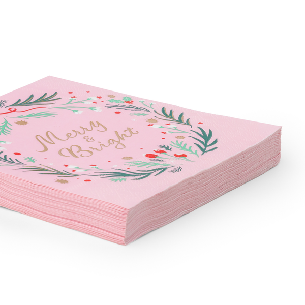 Angled stack of pink Christmas wreath napkins showing the gold "Merry & Bright" lettering and pink-edged depth.